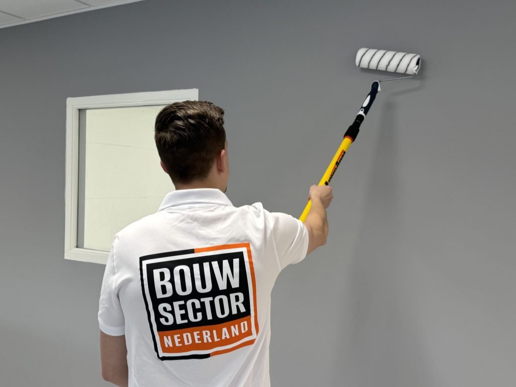 Schilder van Bouwsector Nederland rolt een grijze muur rond een raam met een witte omlijsting