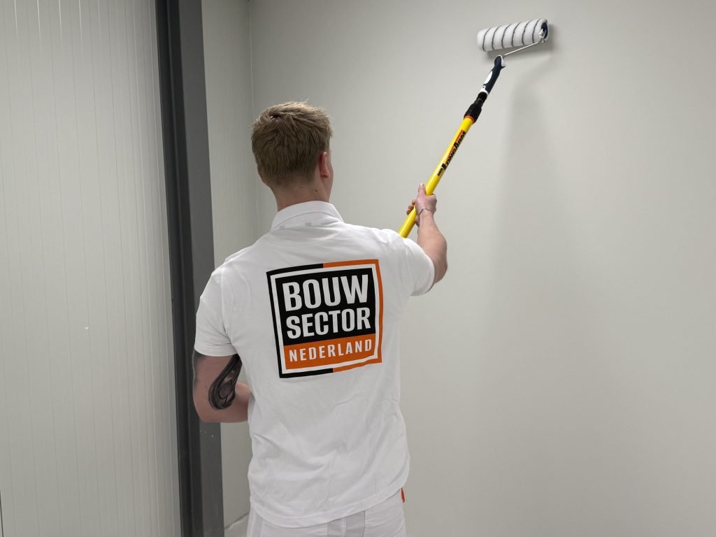 Schilder van Bouwsector Nederland rolt met een lange steel een lichte wand naast een deurpost