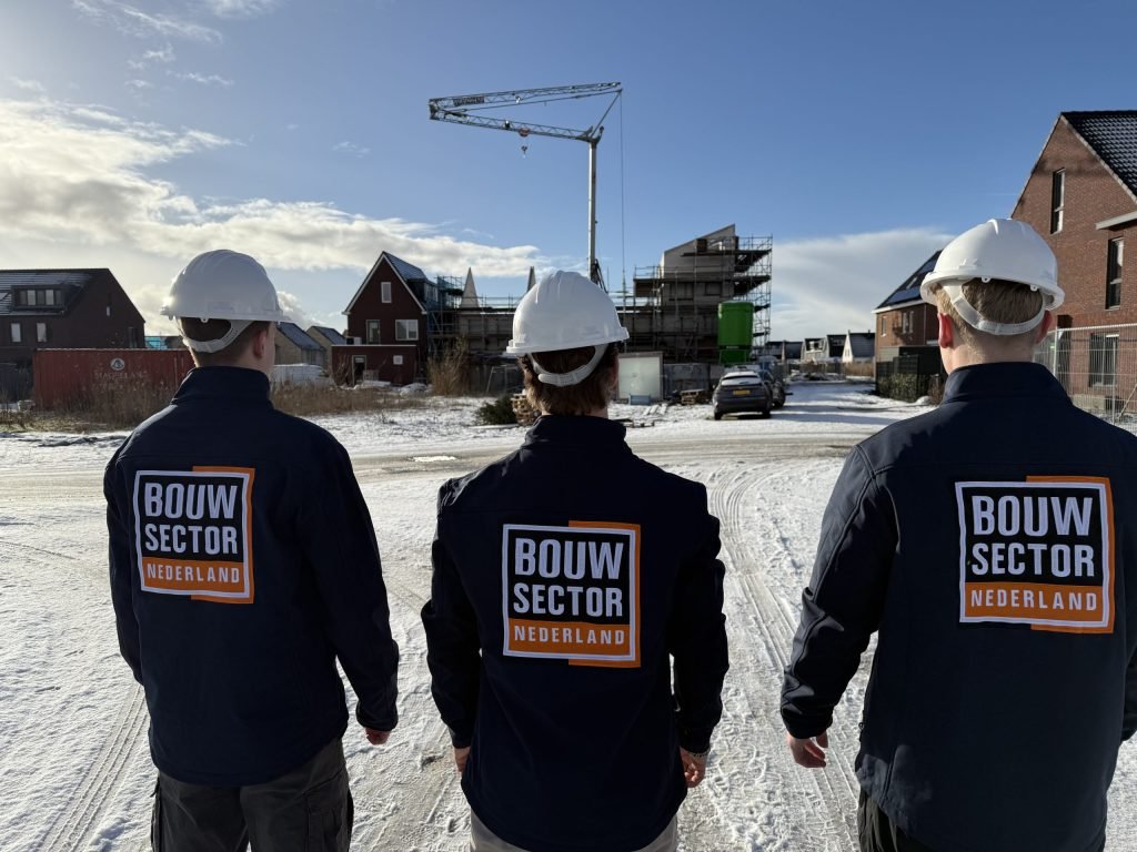 Drie vakmensen van Bouwsector Nederland met witte helm, van achteren gezien, kijken naar nieuwbouwwoningen in aanbouw